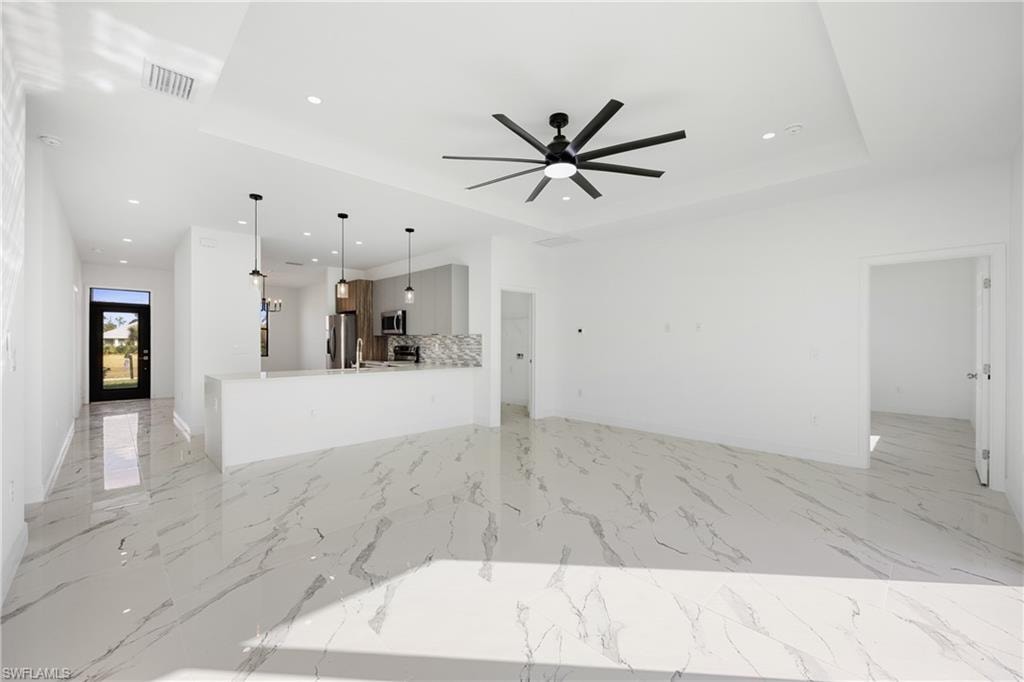 Unfurnished living room with recessed lighting, light marble finish flooring, a ceiling fan, and a tray ceiling