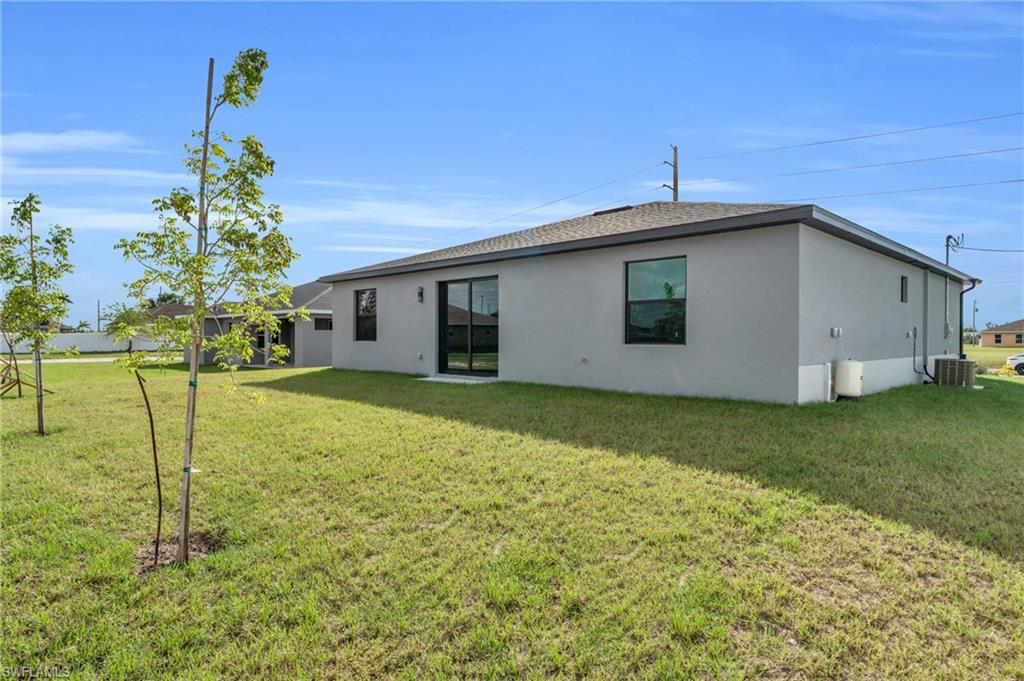 Rear view of property featuring a lawn, stucco siding, and roof with shingles