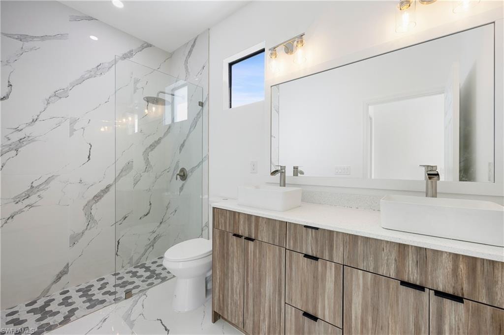 Bathroom featuring double vanity, a marble finish shower, recessed lighting, and light marble finish flooring