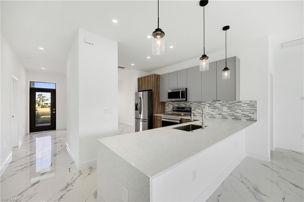 Kitchen with stainless steel appliances, pendant lighting, modern cabinets, recessed lighting, and light stone counters