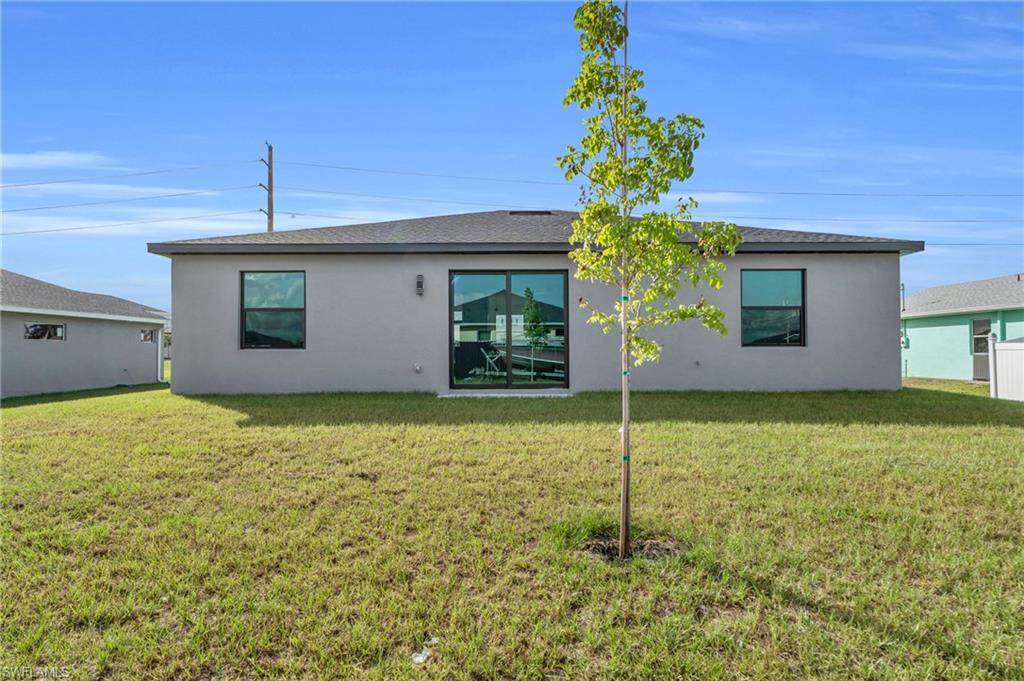Back of property featuring a lawn, stucco siding, and roof with shingles