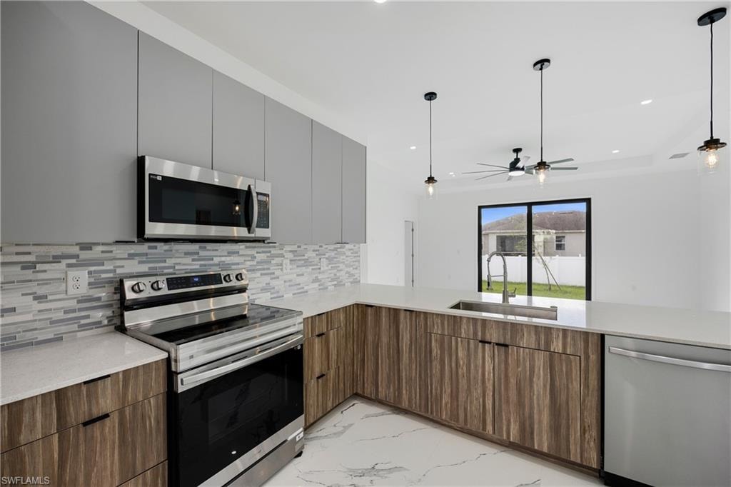 Kitchen featuring appliances with stainless steel finishes, light marble finish floors, modern cabinets, light stone counters, and hanging light fixtures