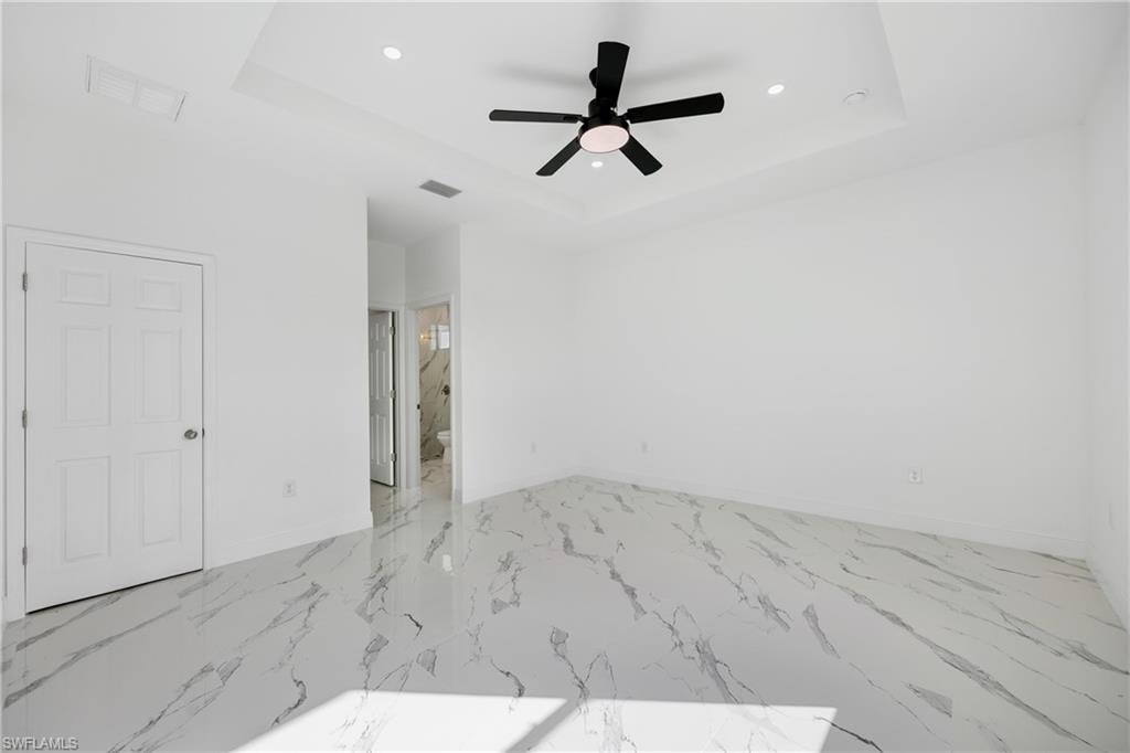 Unfurnished bedroom with a tray ceiling, recessed lighting, marble finish floors, ceiling fan, and ensuite bathroom