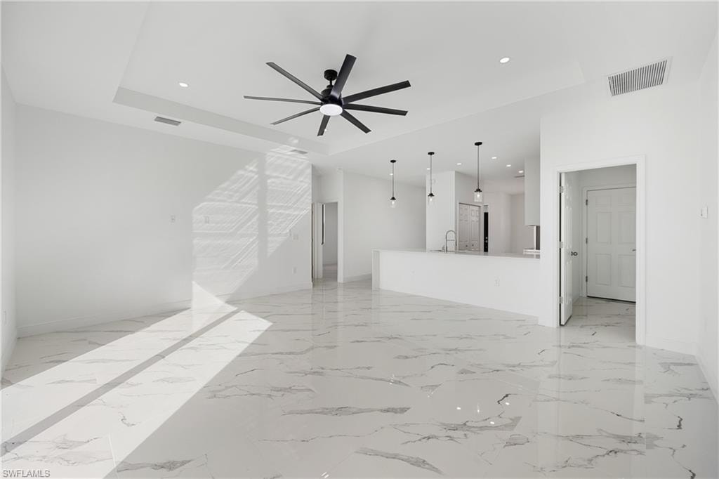 Unfurnished living room with light marble finish flooring, ceiling fan, recessed lighting, and a raised ceiling