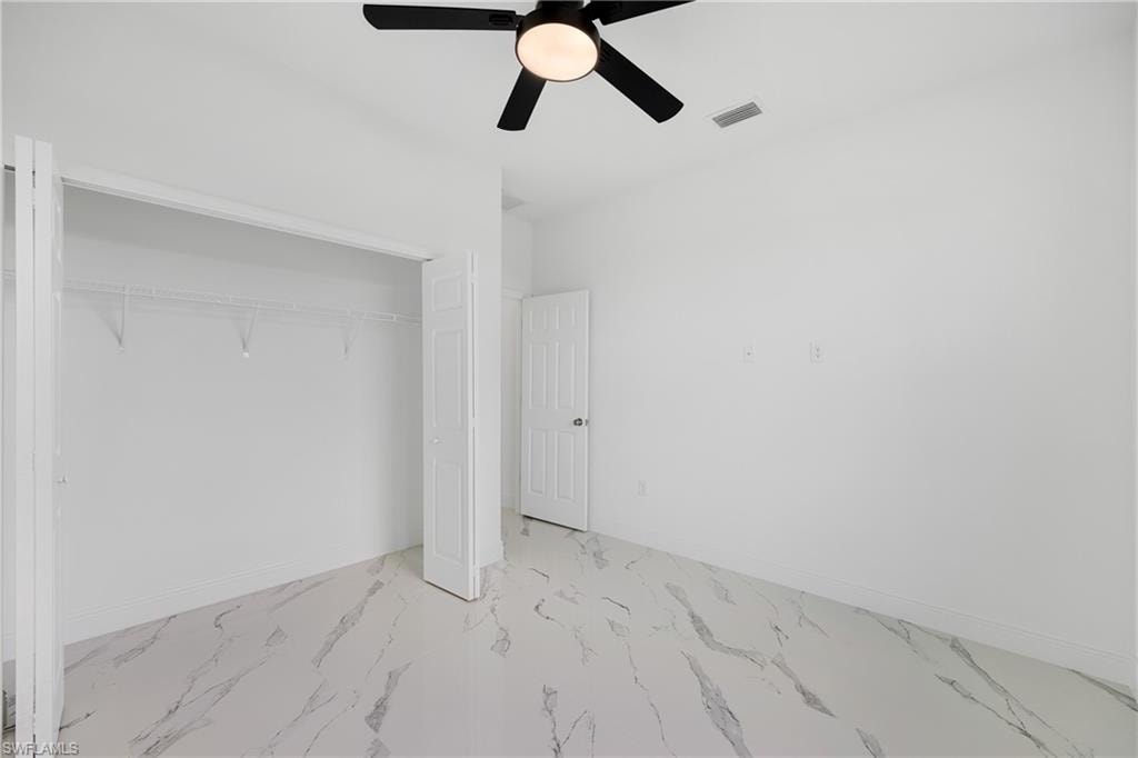 Unfurnished bedroom featuring a closet, light marble finish floors, and a ceiling fan