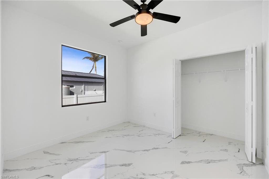 Unfurnished bedroom featuring a ceiling fan, light marble finish flooring, and a closet