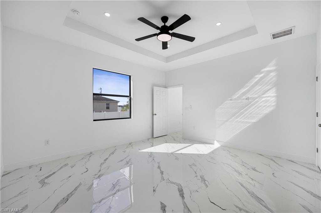 Unfurnished bedroom featuring ceiling fan, light marble finish flooring, a raised ceiling, and recessed lighting