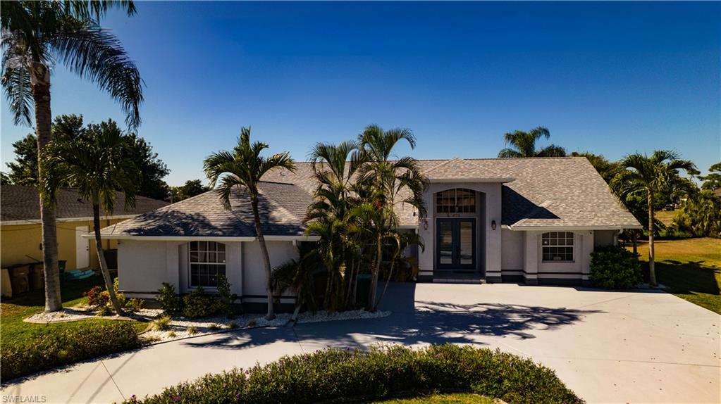View of front of property featuring french doors, driveway, stucco siding, and roof with shingles