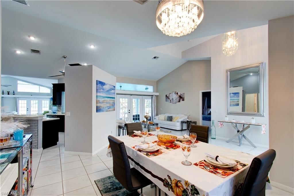 Dining area featuring french doors, light tile patterned floors, a chandelier, and high vaulted ceiling