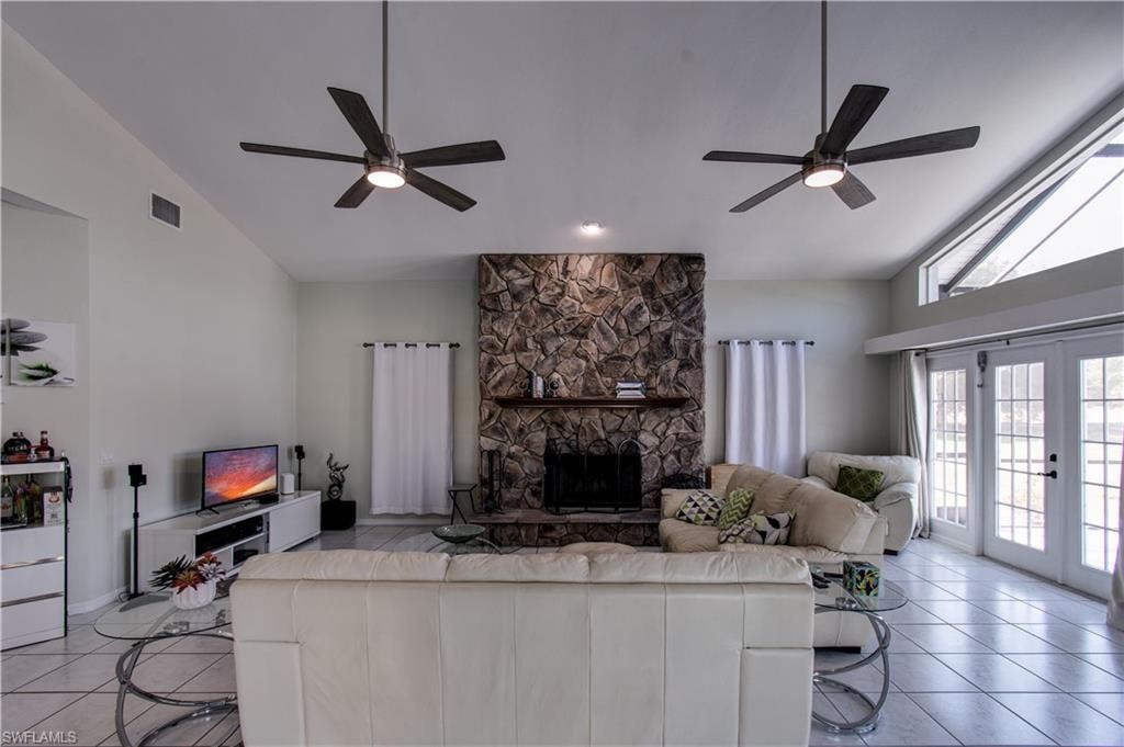 Living area featuring high vaulted ceiling, a fireplace, light tile patterned floors, ceiling fan, and french doors
