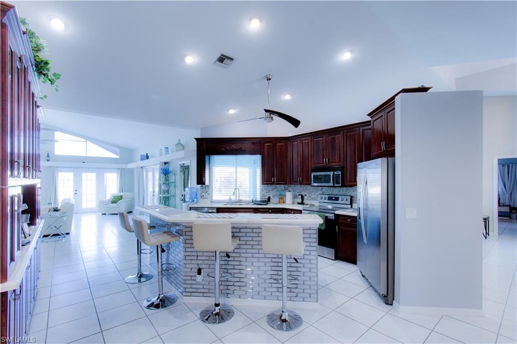 Kitchen featuring light countertops, lofted ceiling, stainless steel appliances, light tile patterned floors, and a kitchen bar