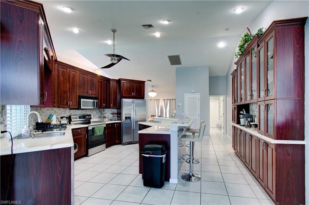 Kitchen with a kitchen bar, appliances with stainless steel finishes, vaulted ceiling, light tile patterned flooring, and a center island