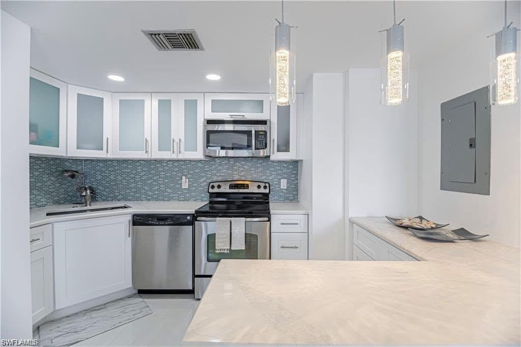 Kitchen featuring stainless steel appliances, glass insert cabinets, white cabinetry, and pendant lighting over spacious island