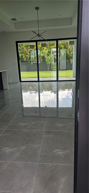 Doorway to outside with healthy amount of natural light, marble look tile flooring, and a raised ceiling