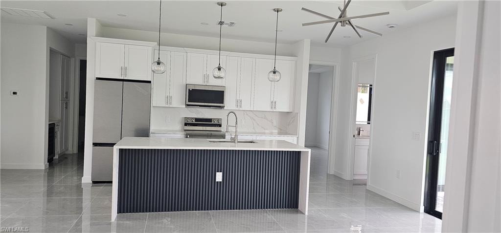 Kitchen with stainless steel appliances, light stone countertops, a kitchen island with sink, pendant lighting, and white cabinetry
