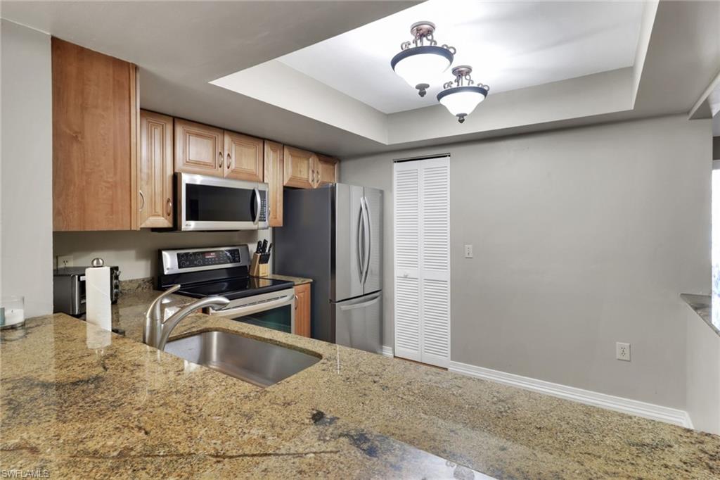 Kitchen featuring a tray ceiling, appliances with stainless steel finishes, and light stone counters