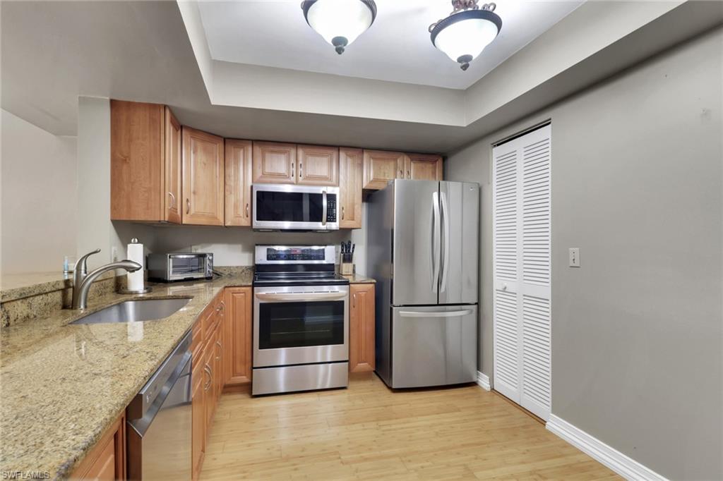 Kitchen with stainless steel appliances, light stone counters, light wood-style flooring, and a tray ceiling