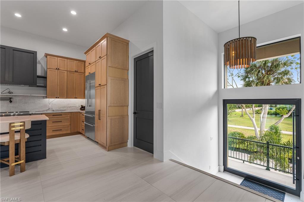 Kitchen with light brown cabinetry, hanging light fixtures, stainless steel built in refrigerator, backsplash, and recessed lighting