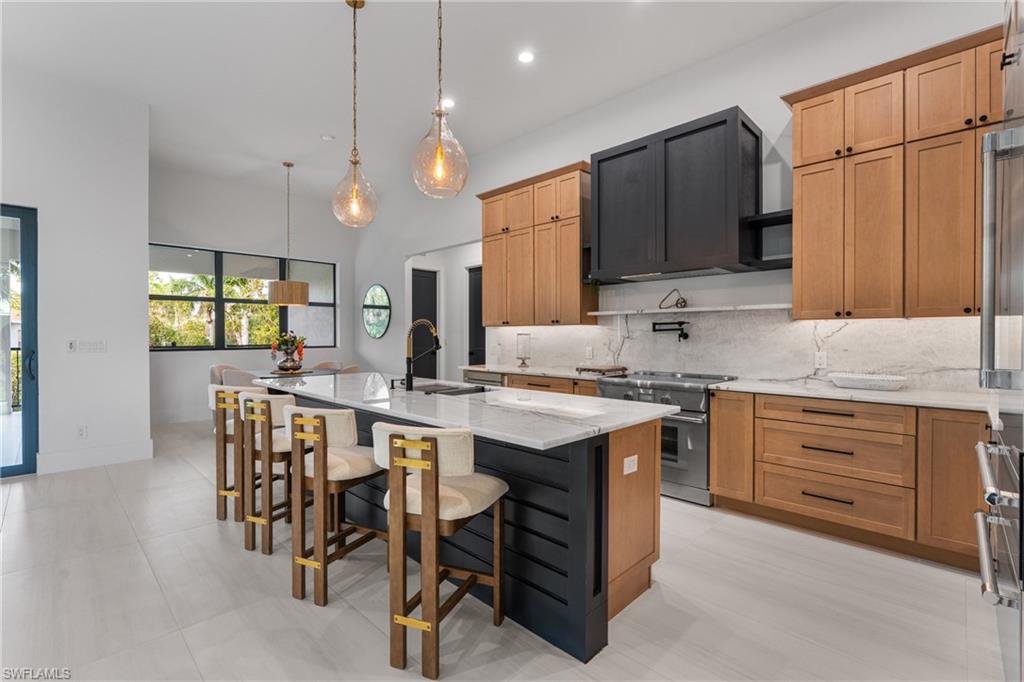 Kitchen featuring light stone counters, a kitchen breakfast bar, decorative backsplash, pendant lighting, and a kitchen island with sink