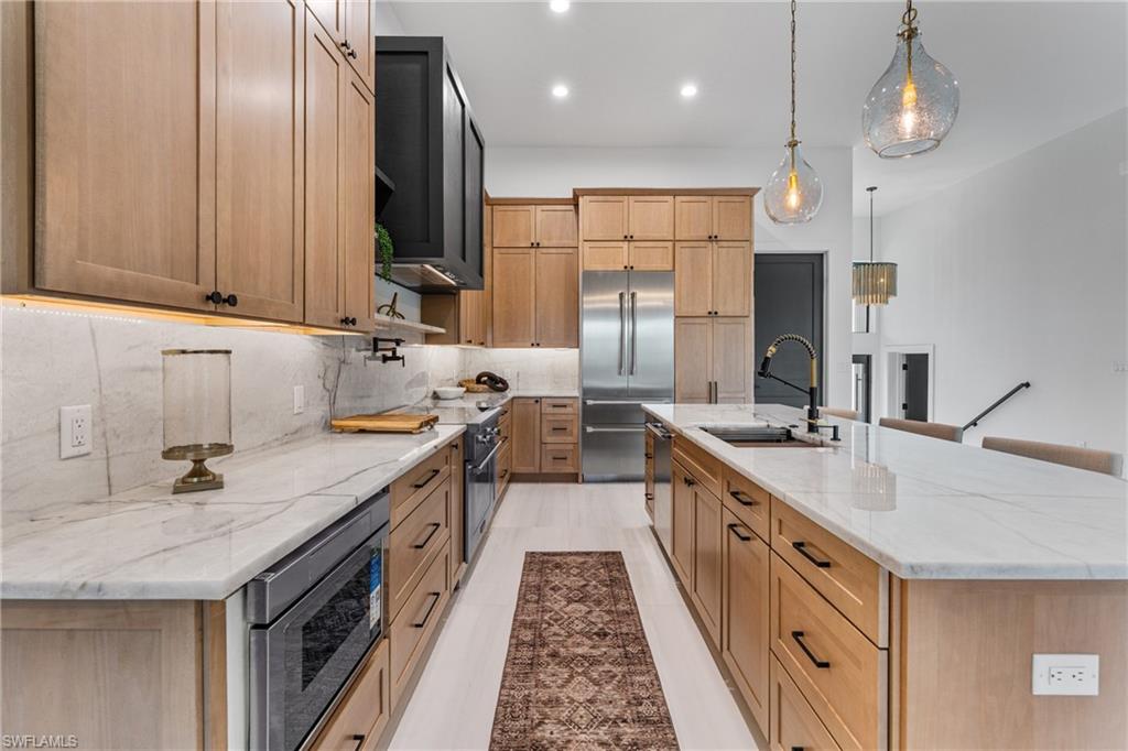 Kitchen featuring light stone counters, recessed lighting, built in appliances, a spacious island, and pendant lighting