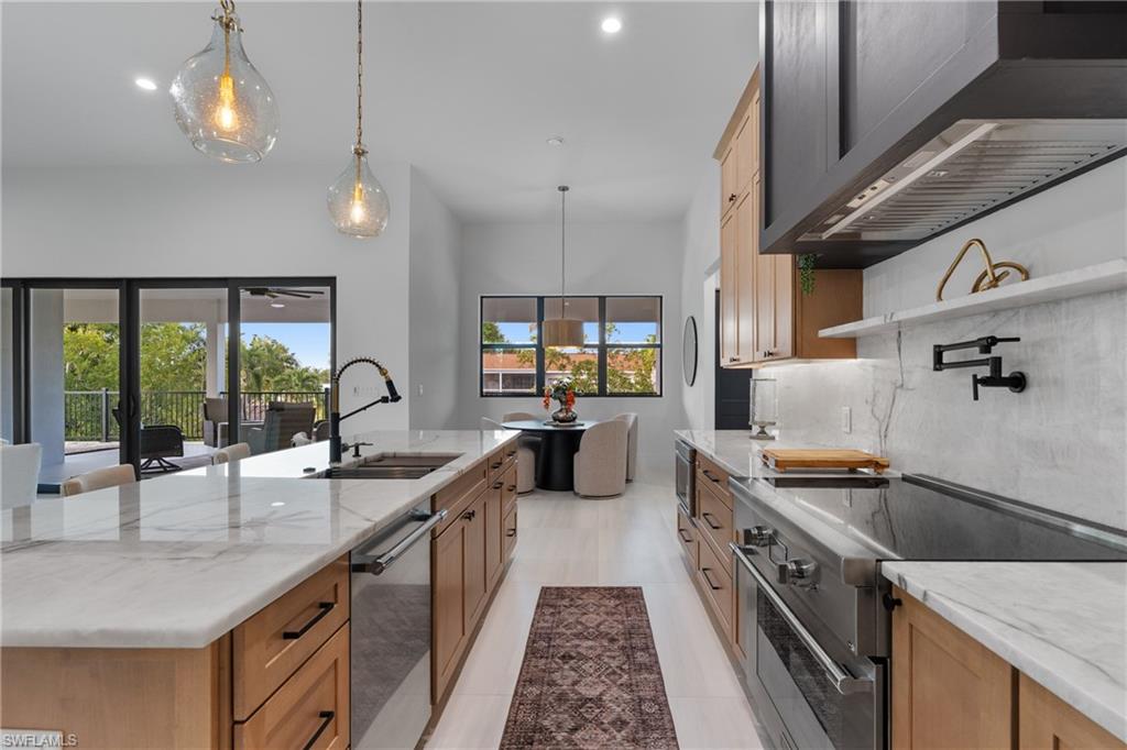 Kitchen featuring light stone countertops, appliances with stainless steel finishes, wall chimney range hood, hanging light fixtures, and recessed lighting