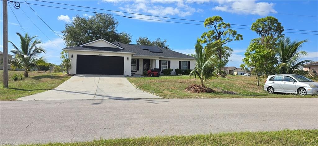 Ranch-style home featuring a front lawn, driveway, a garage, solar panels, and stucco siding