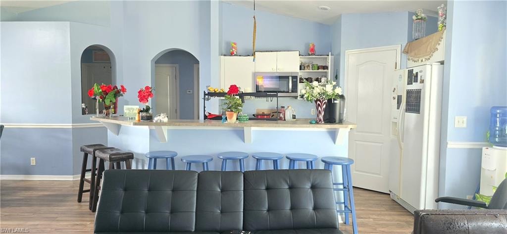Kitchen with white refrigerator with ice dispenser, stainless steel microwave, a peninsula, dark wood finished floors, and a towering ceiling