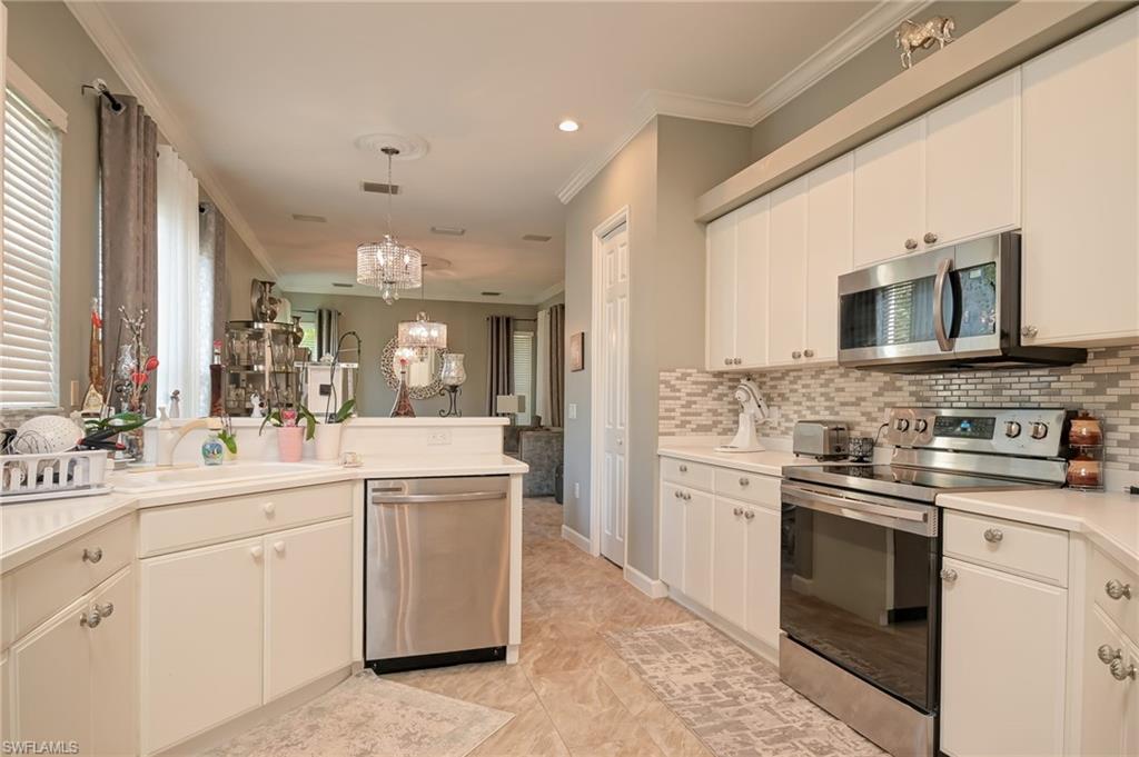 Kitchen with stainless steel appliances, crown molding, light countertops, pendant lighting, and a chandelier