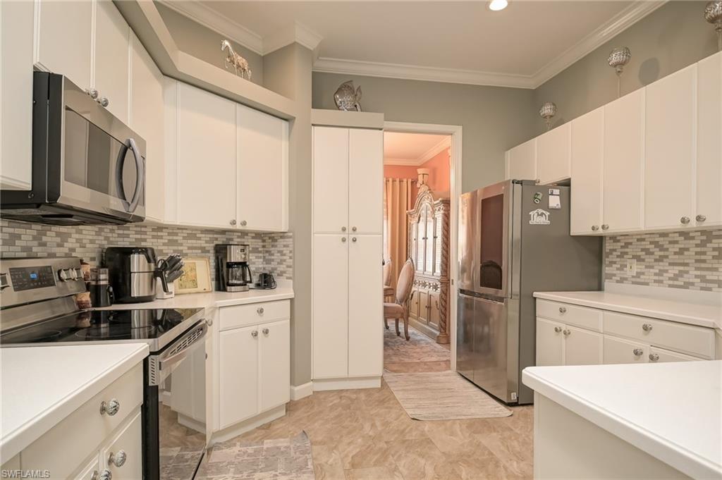 Kitchen with stainless steel appliances, crown molding, backsplash, light countertops, and white cabinets