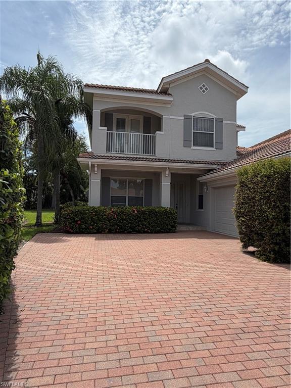 Stucco exterior residence featuring a barrel tile roof, second-story balcony with white railing, decorative window shutters, and an expansive paver driveway