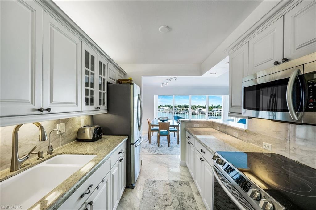 Kitchen featuring decorative backsplash, stainless steel appliances, light stone countertops, and glass insert cabinets
