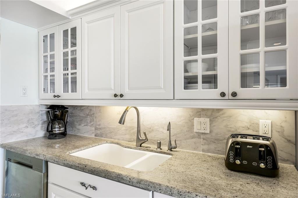Kitchen with glass insert cabinets, white cabinets, light stone countertops, and stainless steel dishwasher