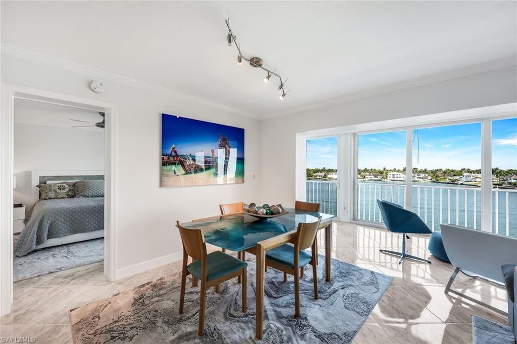 Dining space with light marble finish floors, ornamental molding, a water view, and track lighting