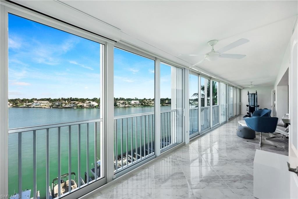 Sunroom with marble tiled flooring, a water view, and a wall of windows