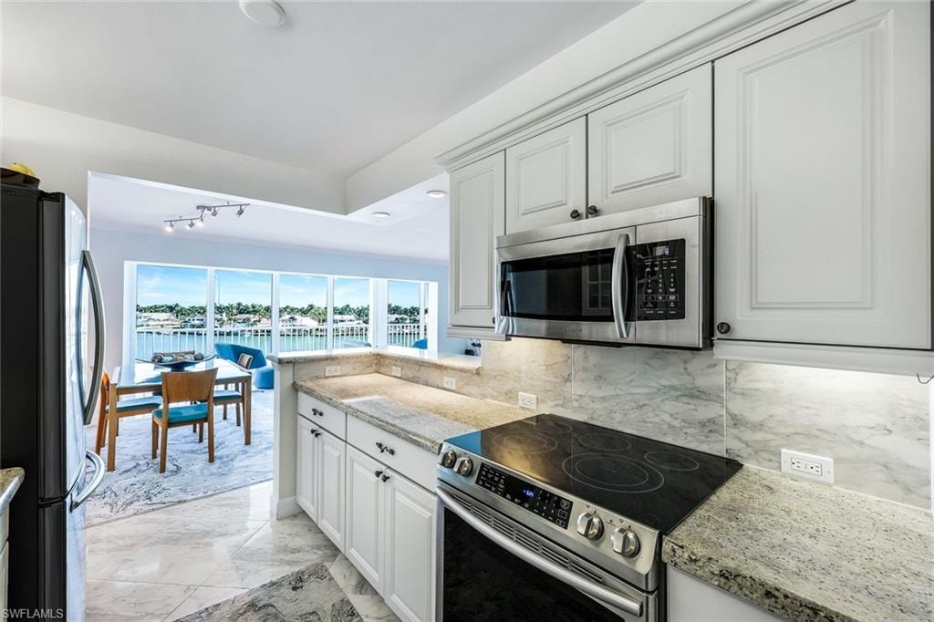 Kitchen featuring stainless steel appliances, light stone counters, light marble finish flooring, white cabinetry, and a water view
