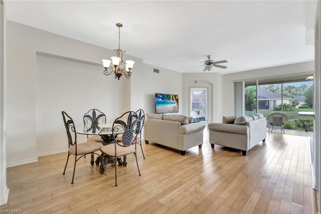 Dining area with light wood-style floors, baseboards, visible vents, and ceiling fan with notable chandelier