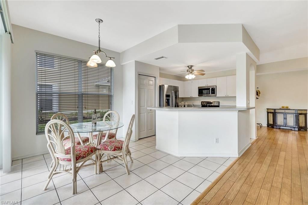 Kitchen with light countertops, hanging light fixtures, appliances with stainless steel finishes, white cabinetry, and ceiling fan