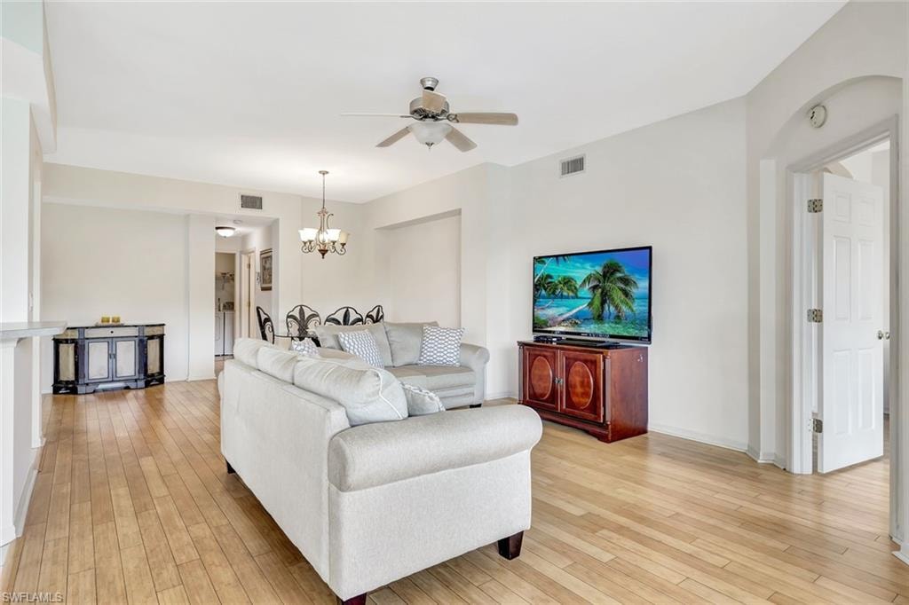 Living room featuring visible vents, light wood-style flooring, and ceiling fan with notable chandelier