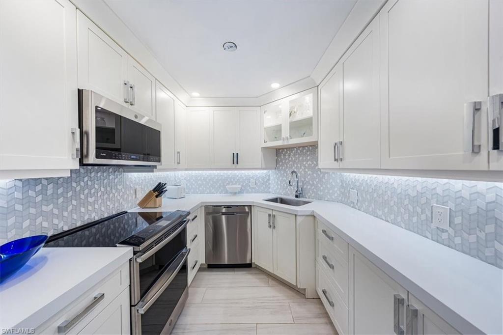 Kitchen featuring stainless steel appliances, tasteful backsplash, light countertops, white cabinetry, and glass insert cabinets