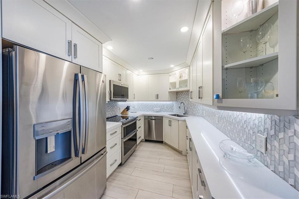Kitchen featuring appliances with stainless steel finishes, light countertops, glass insert cabinets, backsplash, and white cabinets