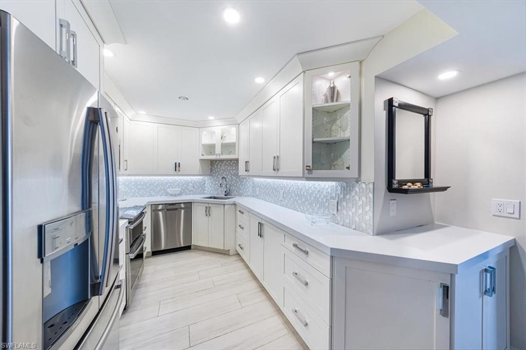 Kitchen with appliances with stainless steel finishes, decorative backsplash, light countertops, glass insert cabinets, and white cabinetry