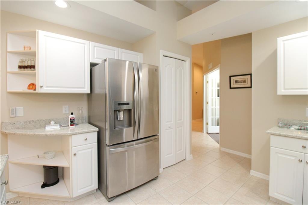 Kitchen with stainless steel fridge, light stone countertops, white cabinetry, and light tile patterned floors