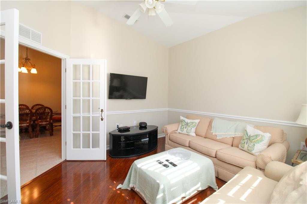 Living room with ceiling fan with notable chandelier, dark wood-type flooring, and vaulted ceiling