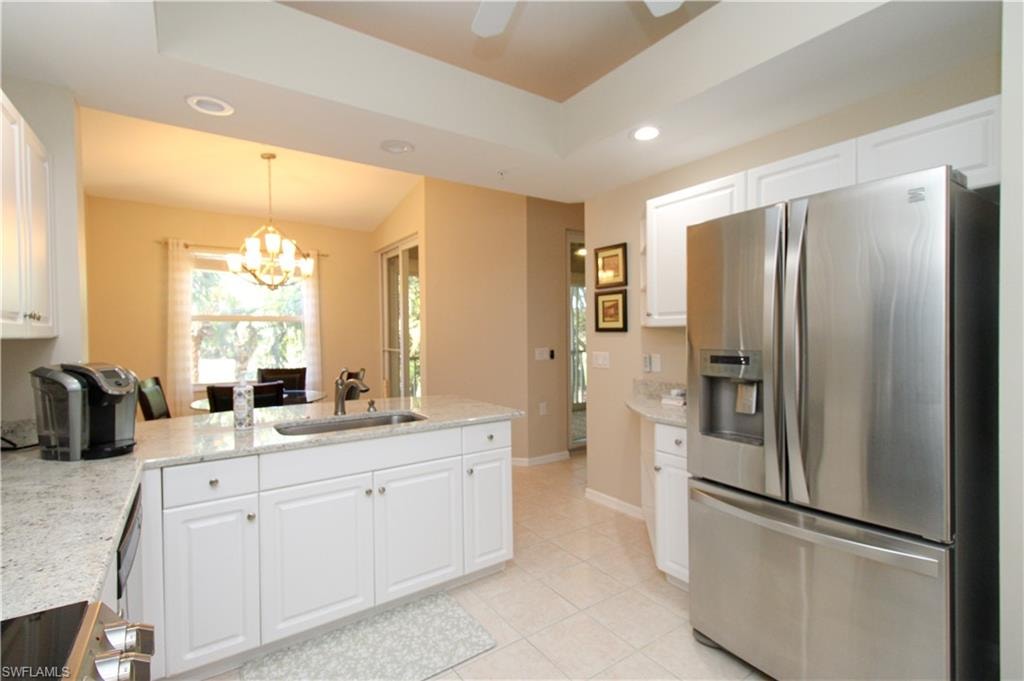 Kitchen with light stone countertops, sink, stainless steel fridge with ice dispenser, a notable chandelier, and white cabinets