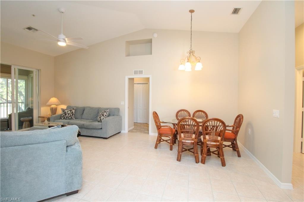 Dining room with light tile patterned floors, ceiling fan with notable chandelier, and lofted ceiling