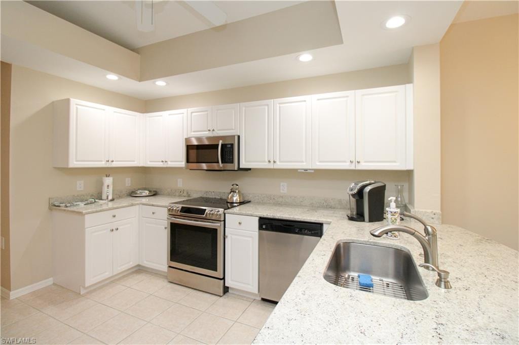 Kitchen with sink, light stone counters, light tile patterned flooring, white cabinets, and appliances with stainless steel finishes