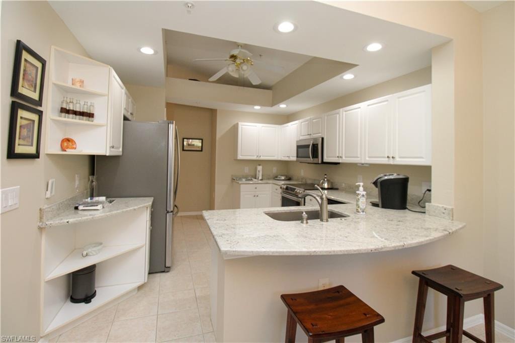 Kitchen with white cabinetry, kitchen peninsula, light stone countertops, and appliances with stainless steel finishes
