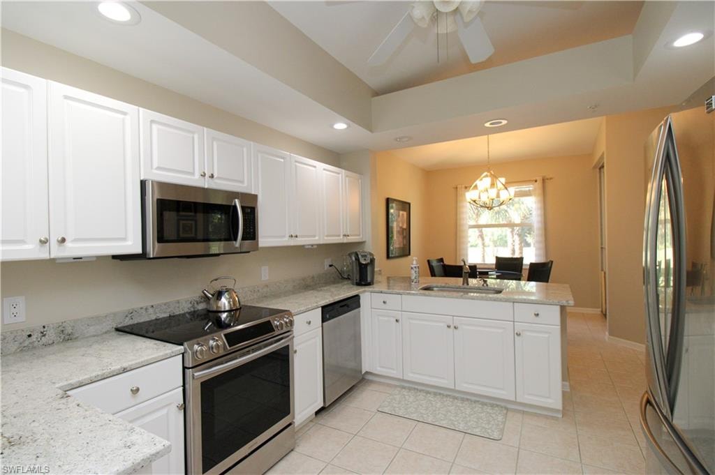Kitchen featuring kitchen peninsula, white cabinetry, stainless steel appliances, and decorative light fixtures