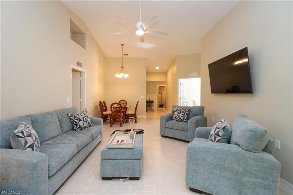 Tiled living room featuring ceiling fan with notable chandelier and a towering ceiling
