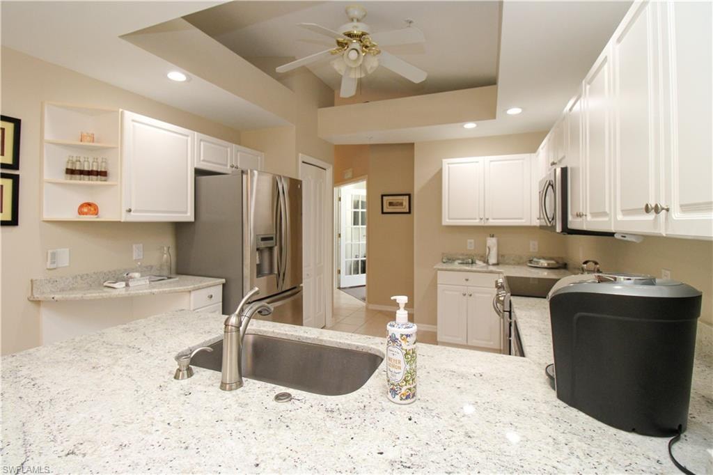 Kitchen featuring light stone counters, stainless steel appliances, ceiling fan, sink, and white cabinetry